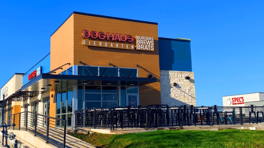 Exterior of Dog Haus Biergarten restaurant with outdoor seating under blue sky.