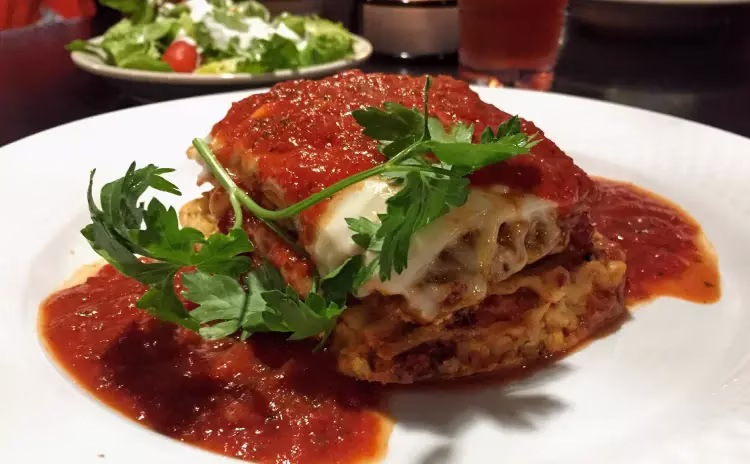 A serving of lasagna topped with red sauce, melted cheese, and parsley.
