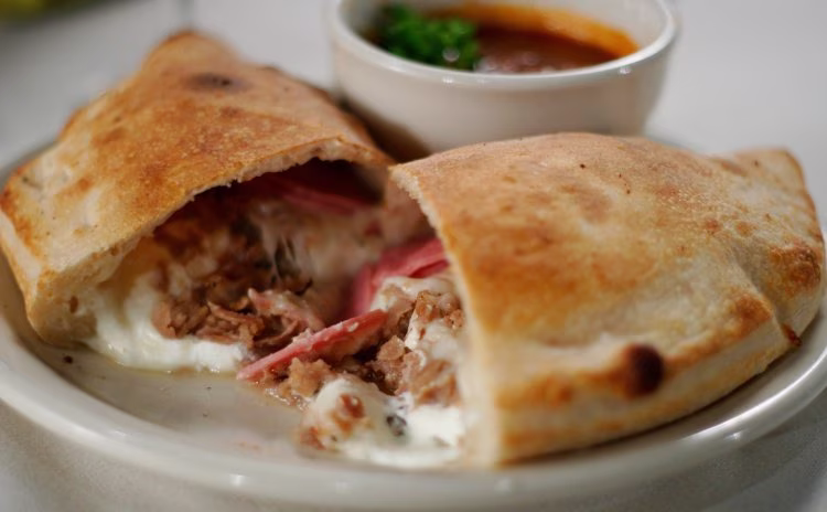 Calzone cut open, revealing meat and cheese filling, with sauce.