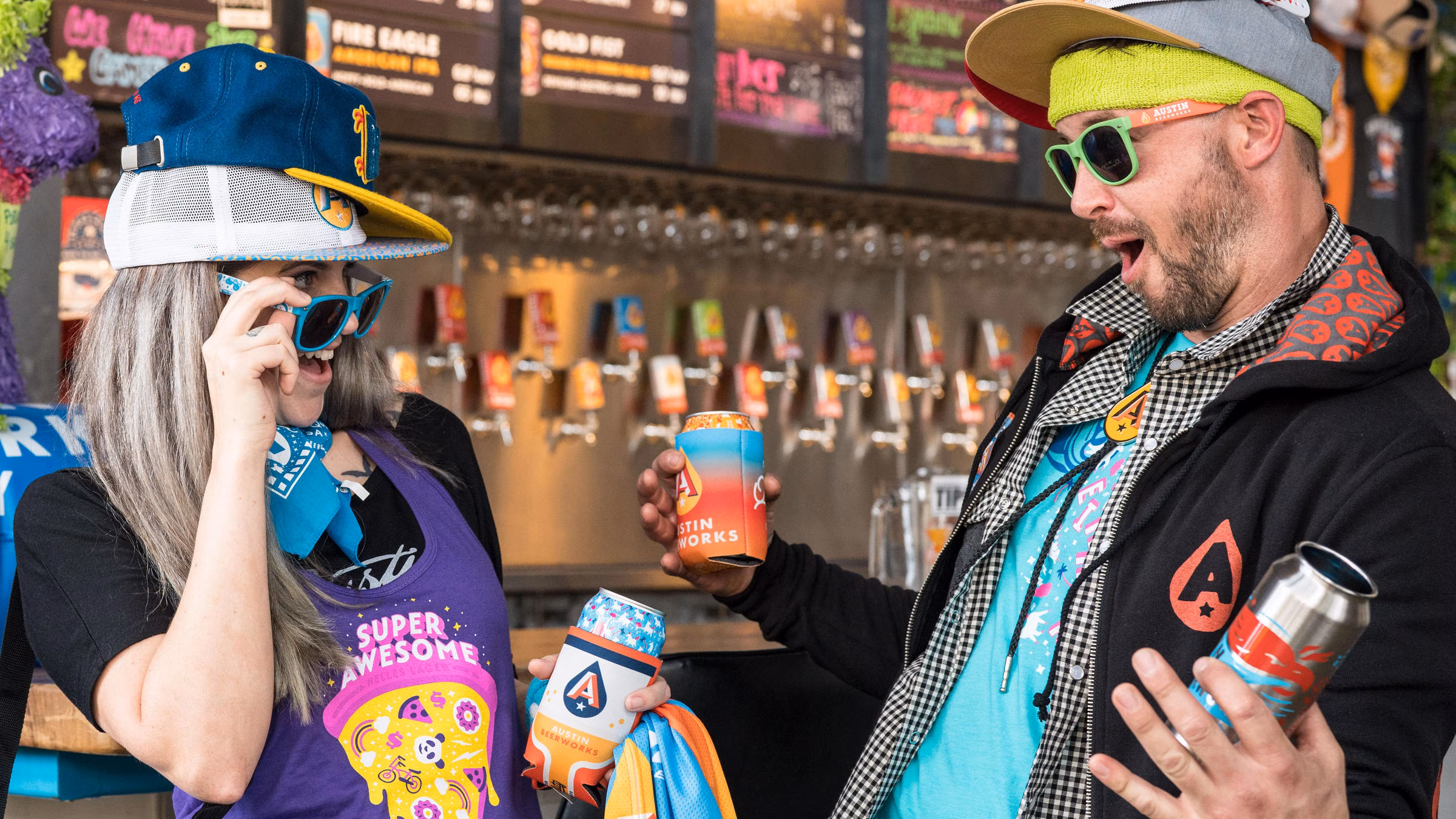 Two people wearing multiple hats and sunglasses holding Austin Beerworks cans.