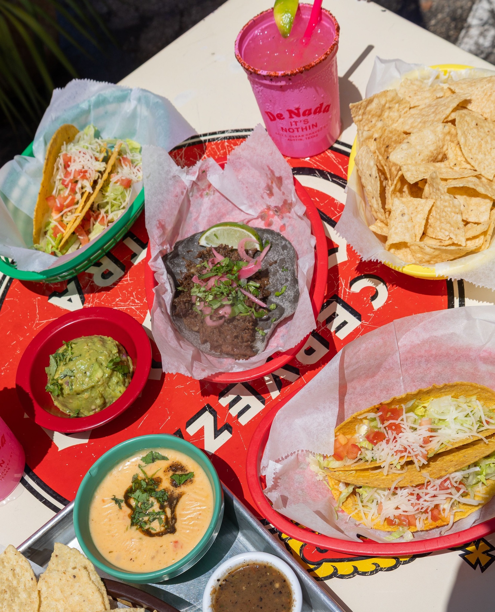 Tacos, tortilla chips, guacamole, queso, and pink drink on table.