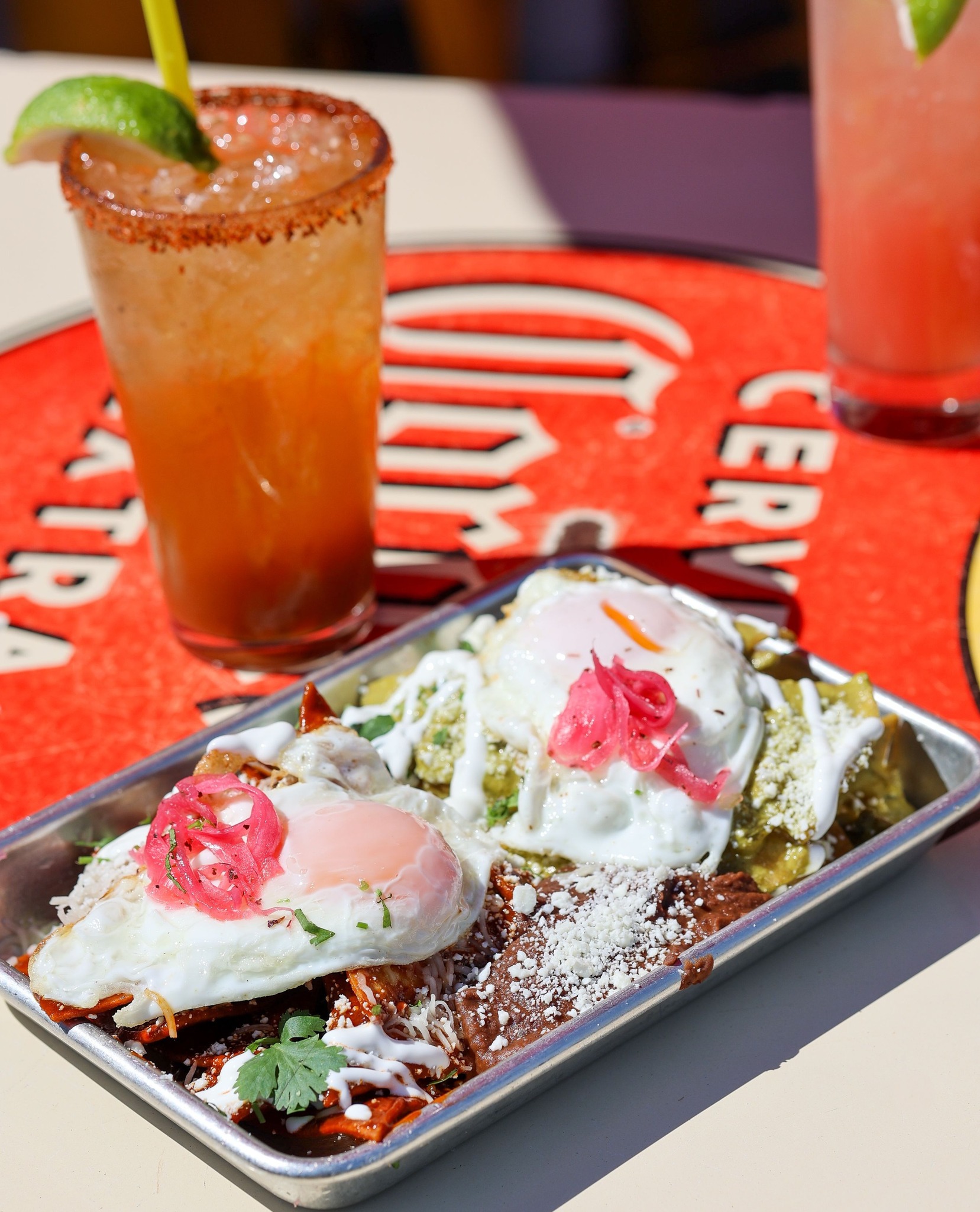 Metal tray of chilaquiles with fried eggs, pickled onions, and drinks.
