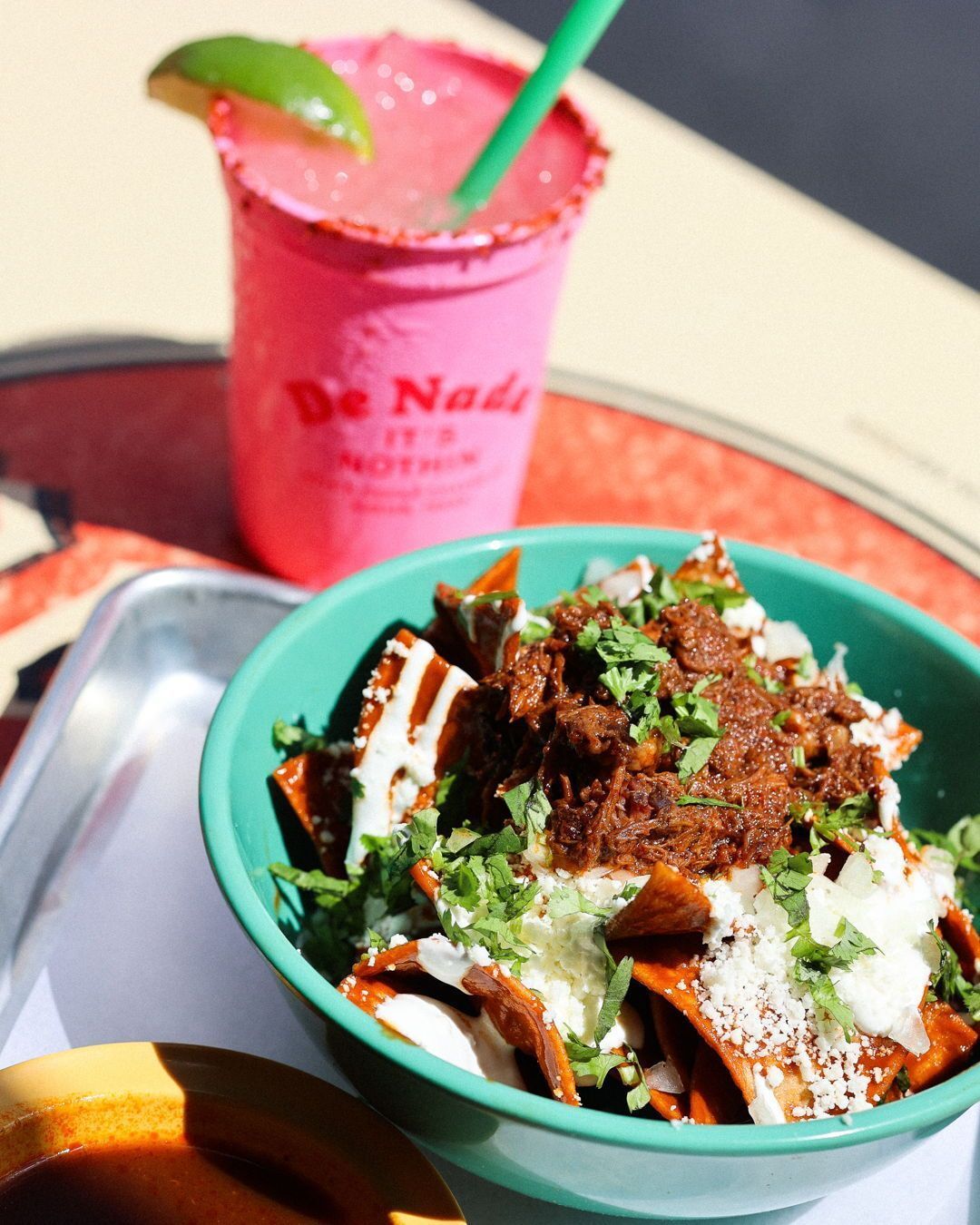 Tortilla chips with meat, cheese, sauce, cilantro; pink drink with lime.