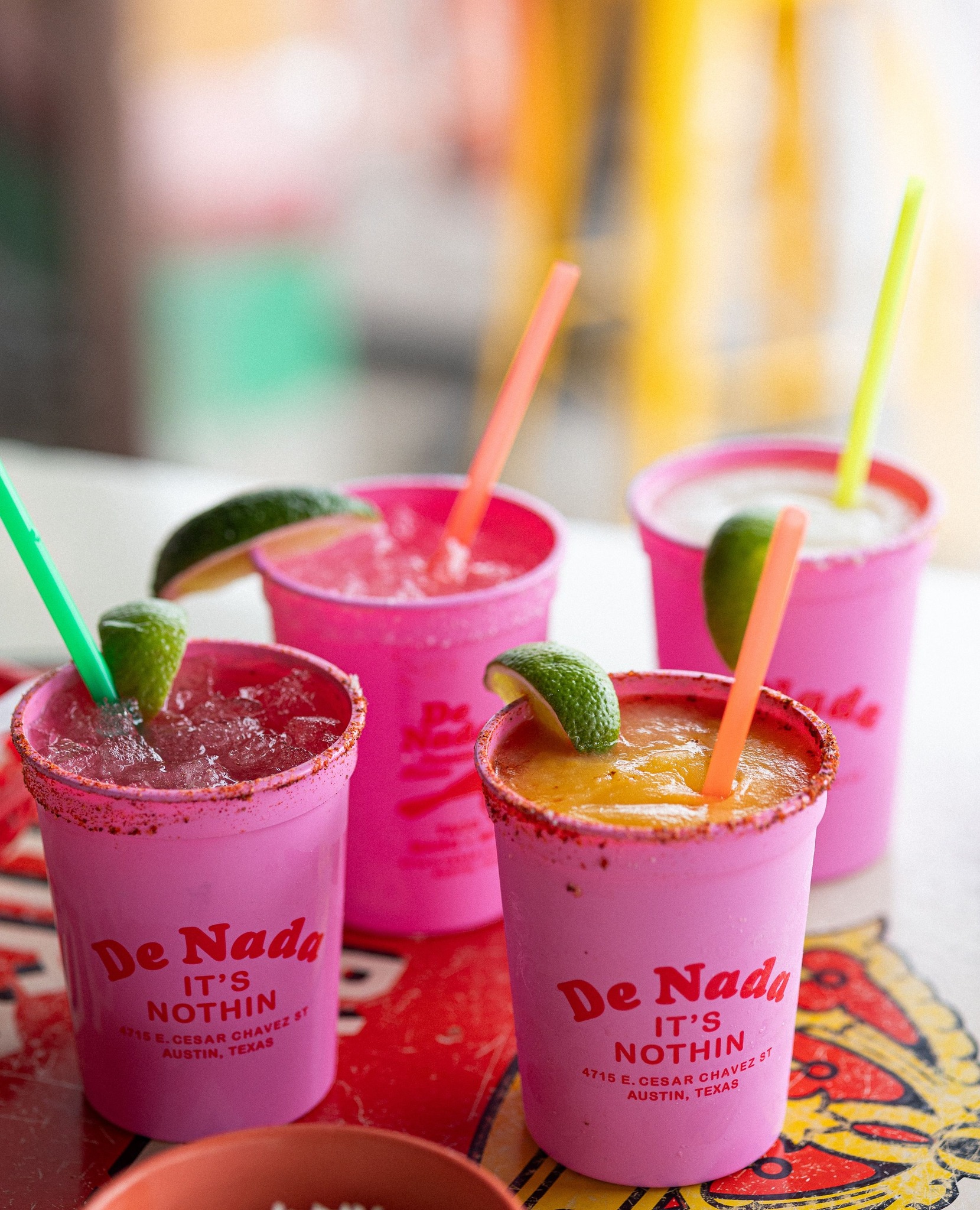 Four pink cups of various iced drinks with lime and straws.