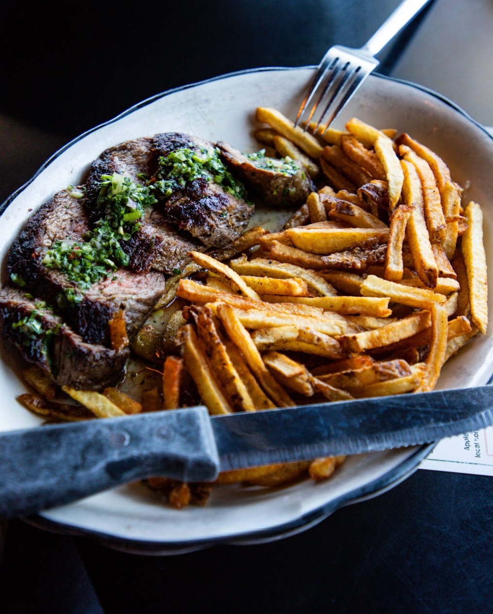 Sliced steak with green sauce and french fries on a plate.
