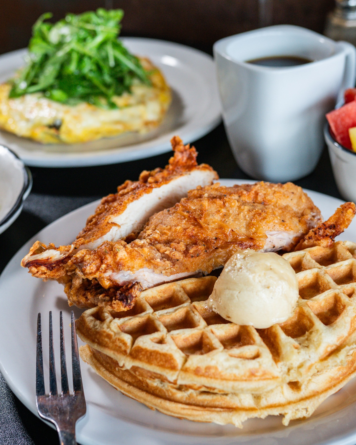 Fried chicken and waffles, omelet with greens, coffee, and fruit.