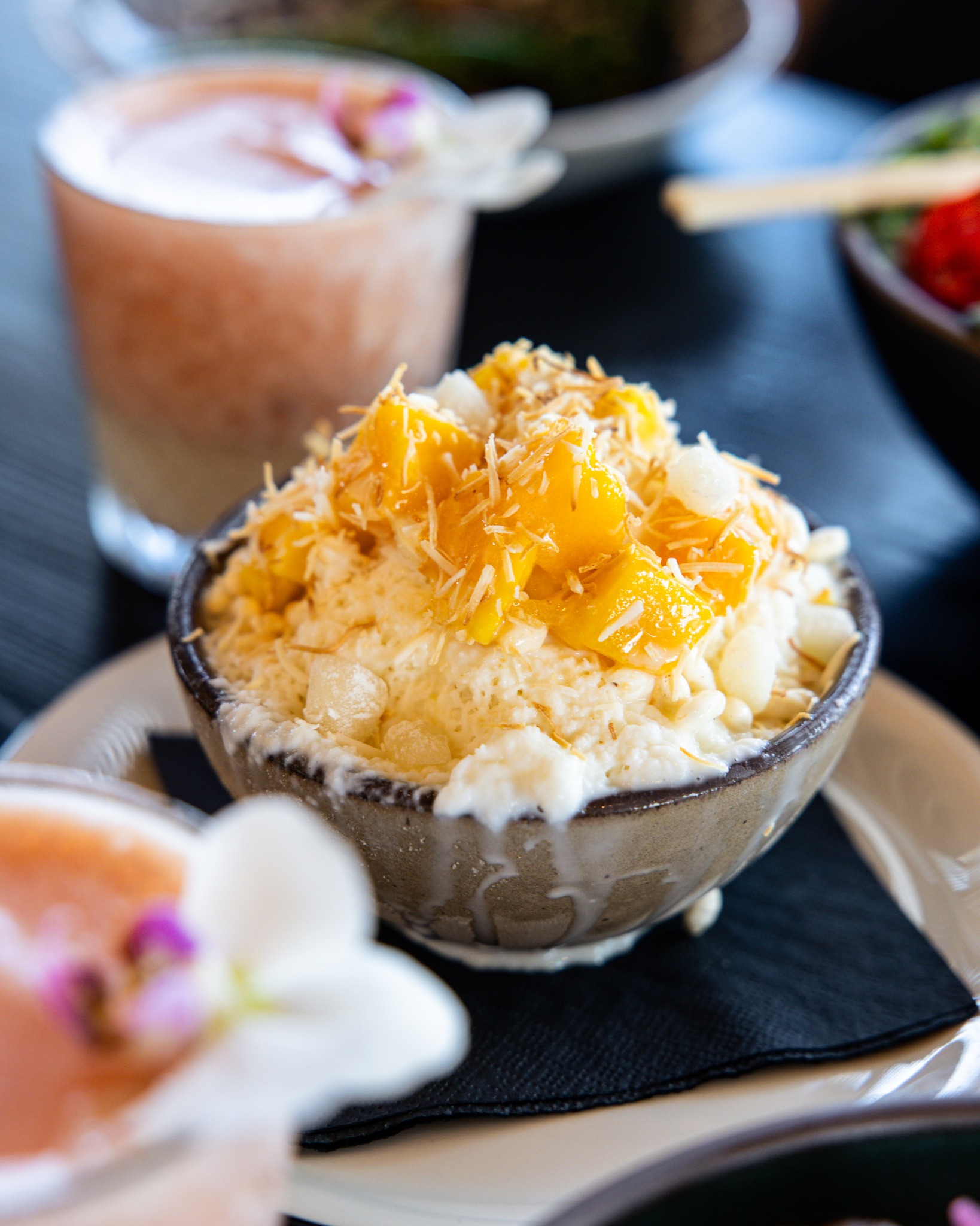 Bowl of creamy dessert topped with mango and toasted coconut.