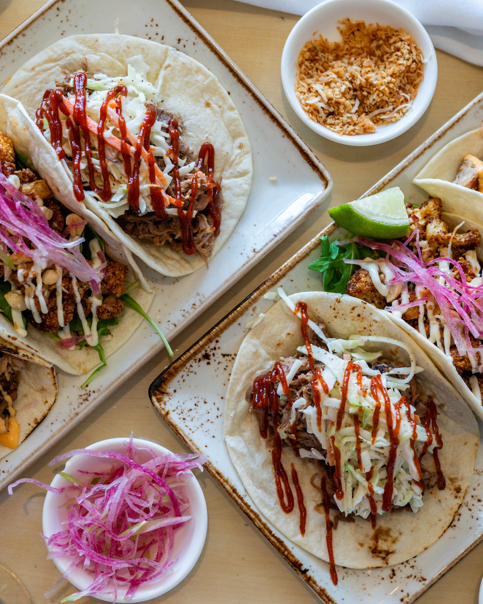 Overhead shot of various tacos with slaw, sauce, and pickled onions.