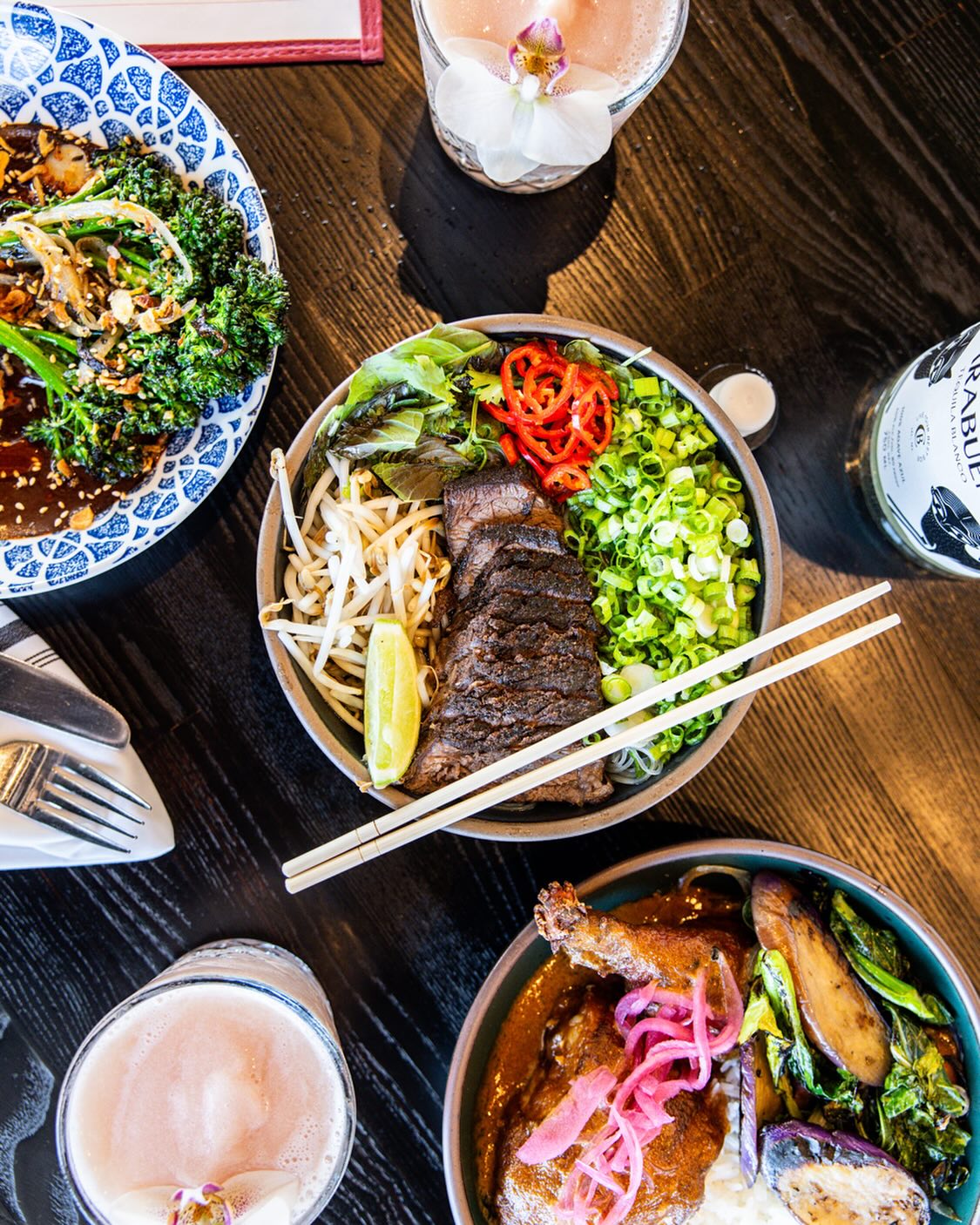 Three bowls of diverse food, two cocktails, and tequila bottle on table.