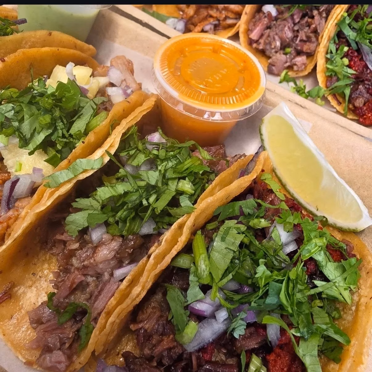 Tacos filled with meat, topped with cilantro, onions, sauce, and lime.