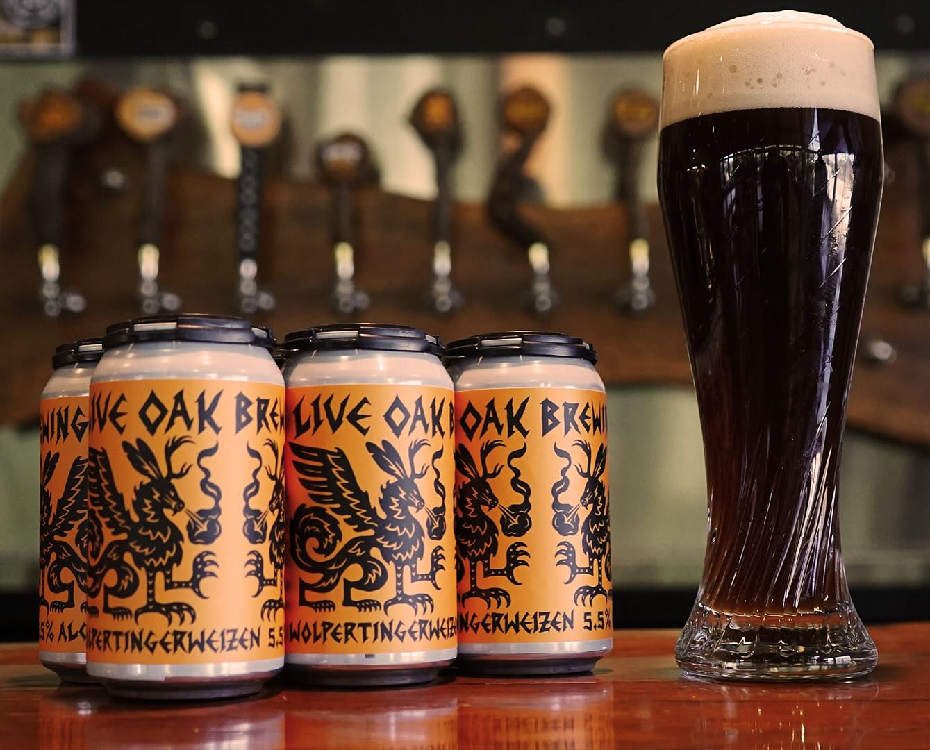 Tall glass of dark beer next to Wolpertingerweizen beer cans.