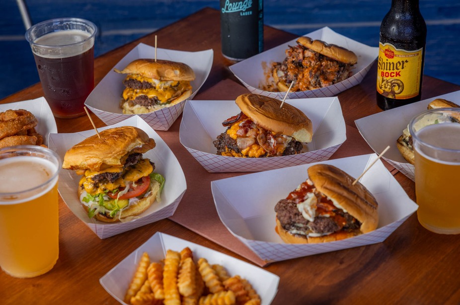Multiple burgers, fries, onion rings, and beers on a wooden table.