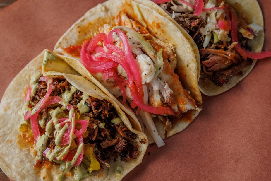 Three tacos with assorted fillings, sauces, and pickled red onions.