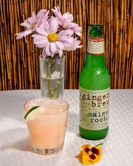 Pink drink with lime, ginger brew bottle, pink flowers, yellow pansy.