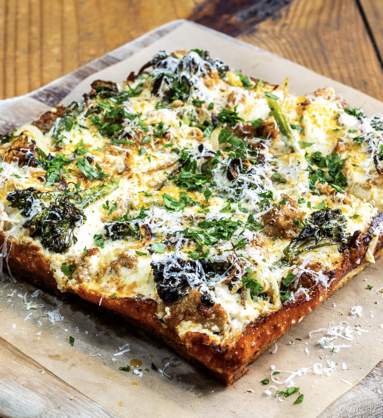 Rectangular deep-dish pizza with cheese, sausage, roasted broccolini, and herbs.