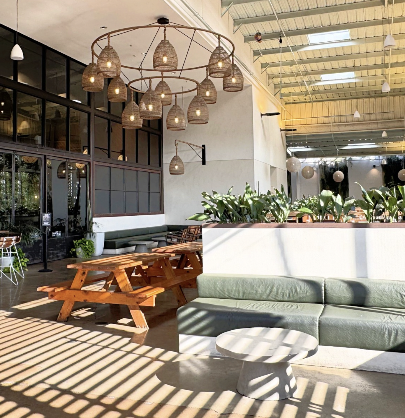 A cafe with picnic tables, green couches, and woven pendant lights.