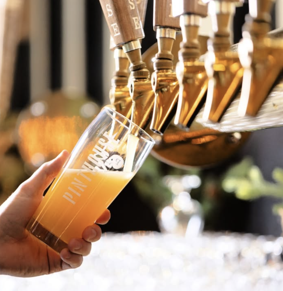 Hand filling a Pinthouse glass with beer from golden taps.