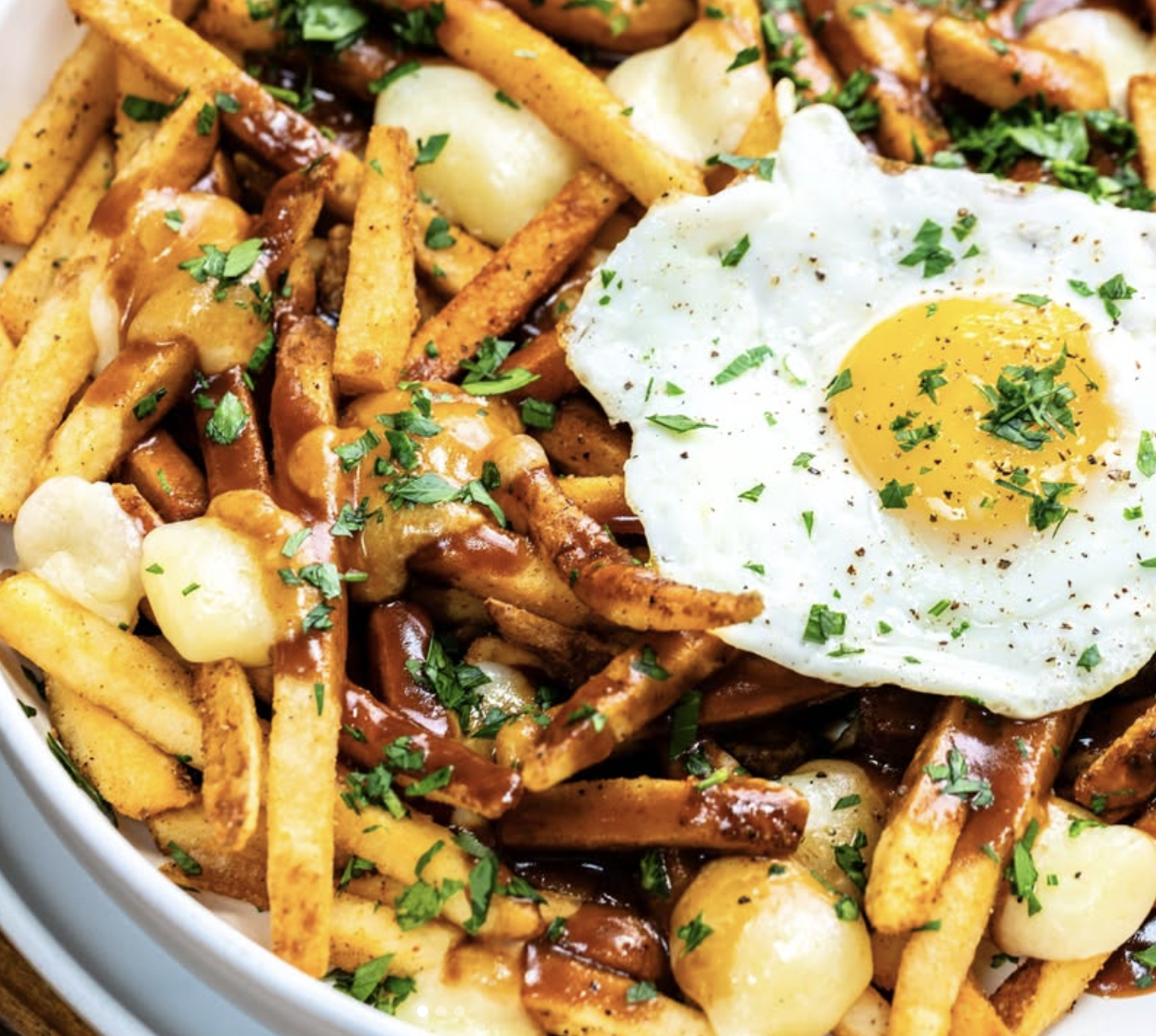 French fries, gravy, cheese curds, and a fried egg with herbs.