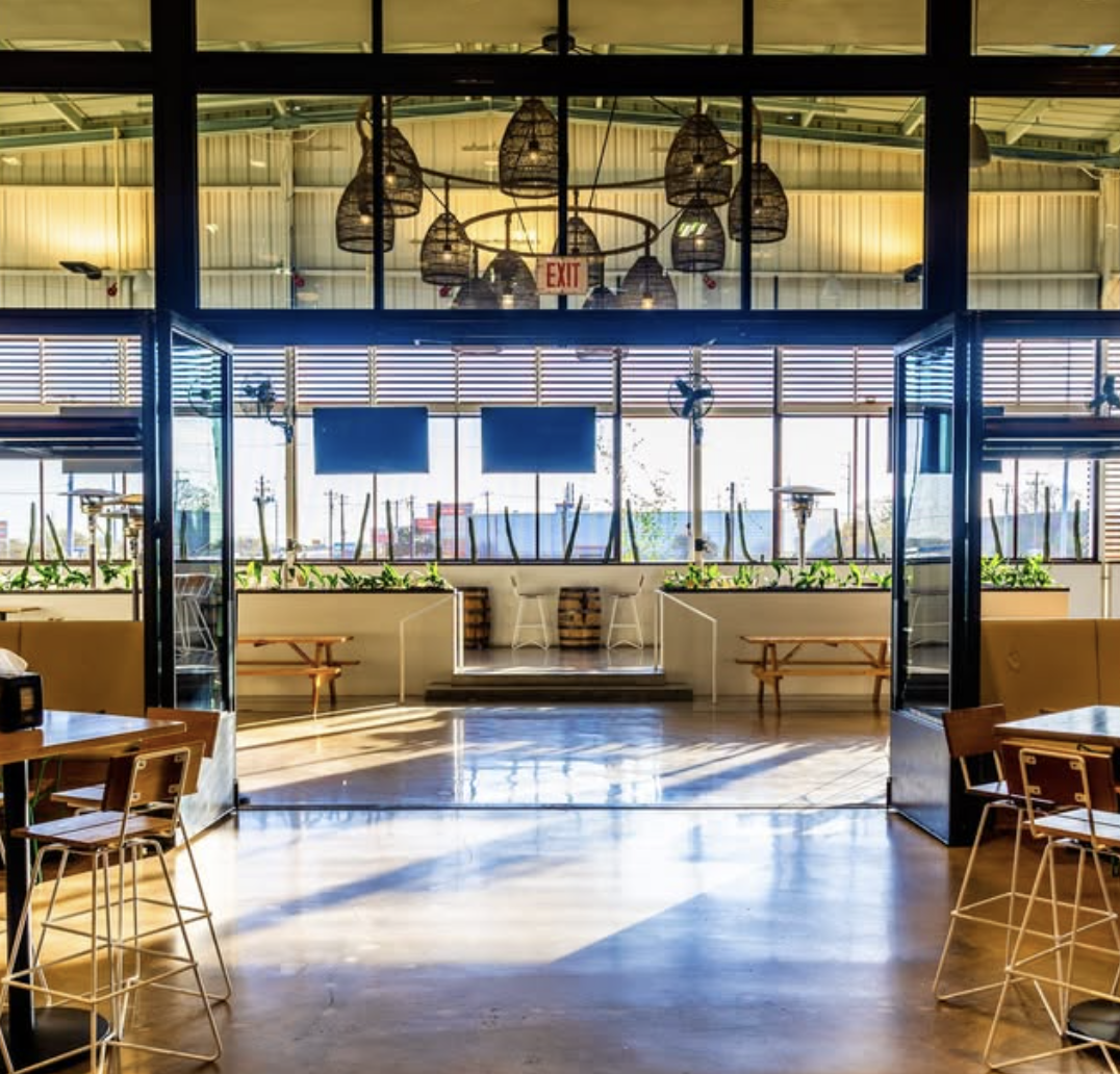 Spacious restaurant interior with concrete floor, large windows, and woven chandeliers.