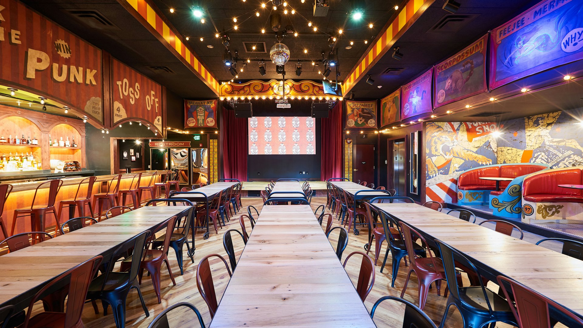 Spacious carnival-themed room with bar, stage, long tables, and booth seating.