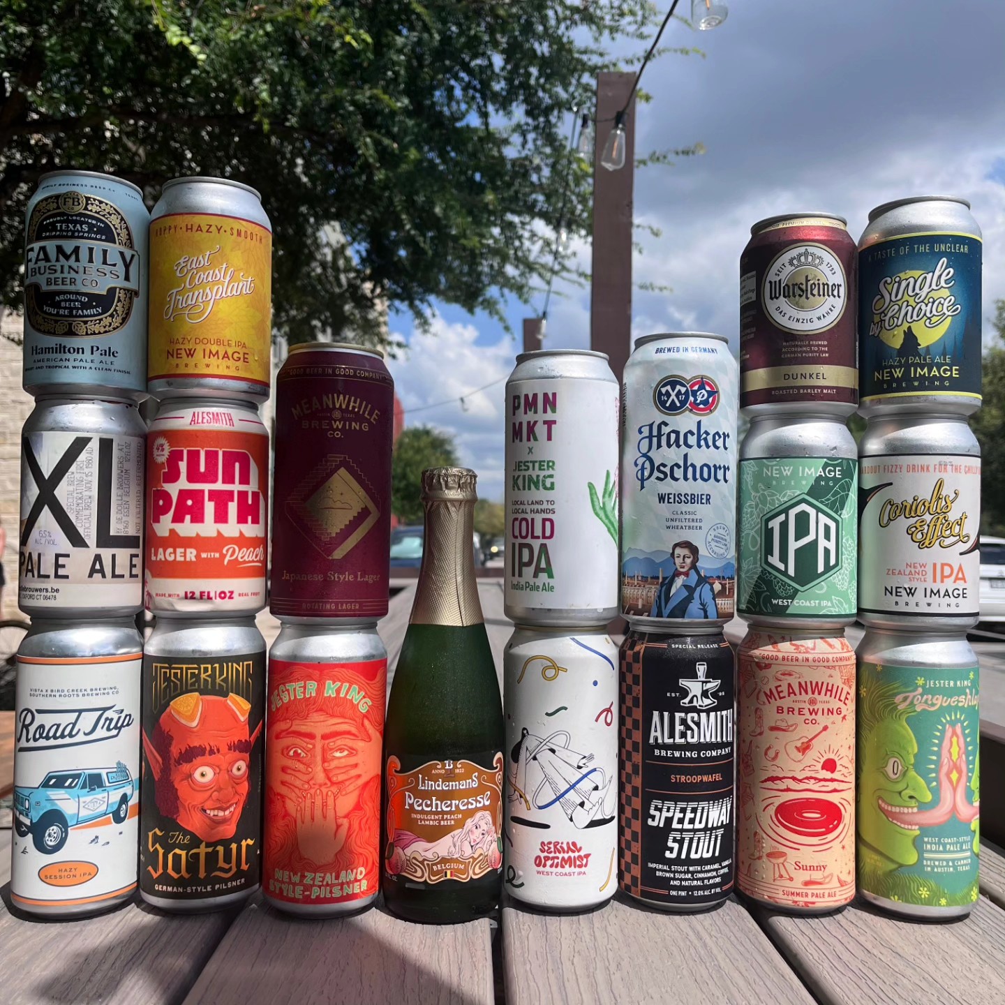 Numerous beer cans and one champagne-style bottle on an outdoor table.