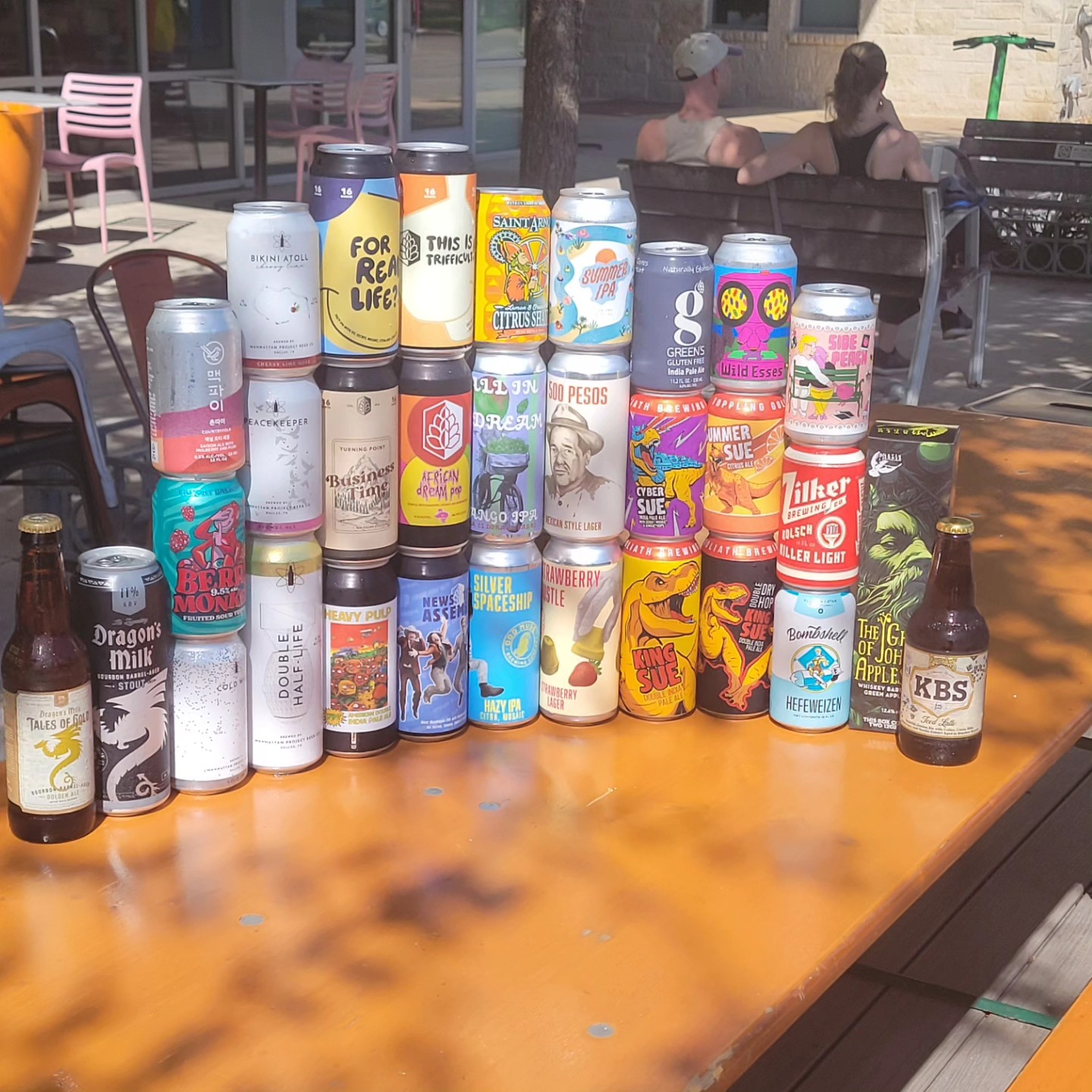 Assorted beer cans and bottles on an outdoor table in sunlight.