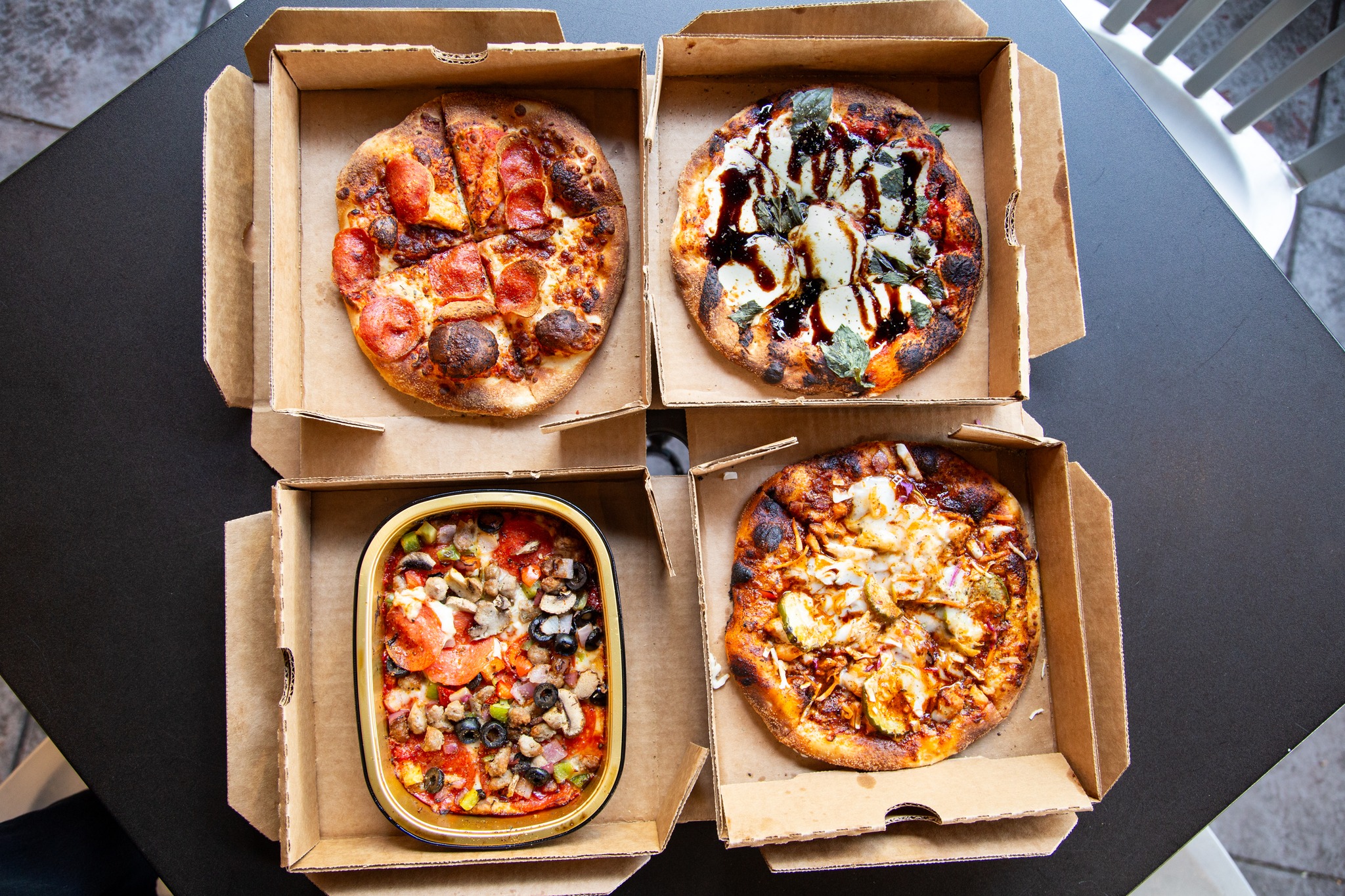 Four pizzas, one rectangular, in open takeout boxes on a table.
