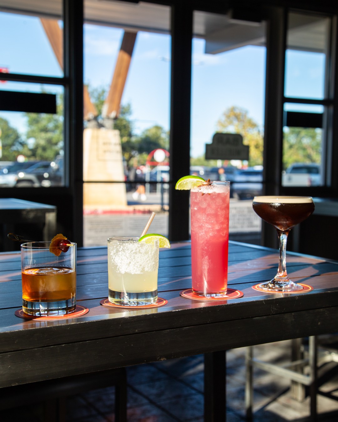 Four different cocktails on a table in front of large windows.