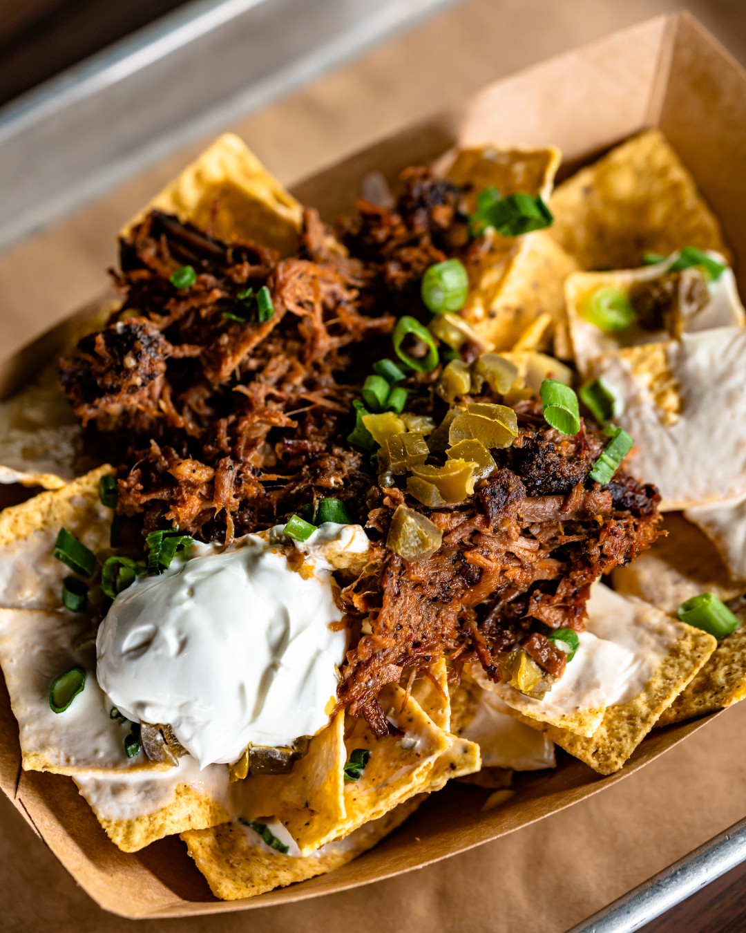 Pulled pork nachos with sour cream, jalapeños, and green onions.