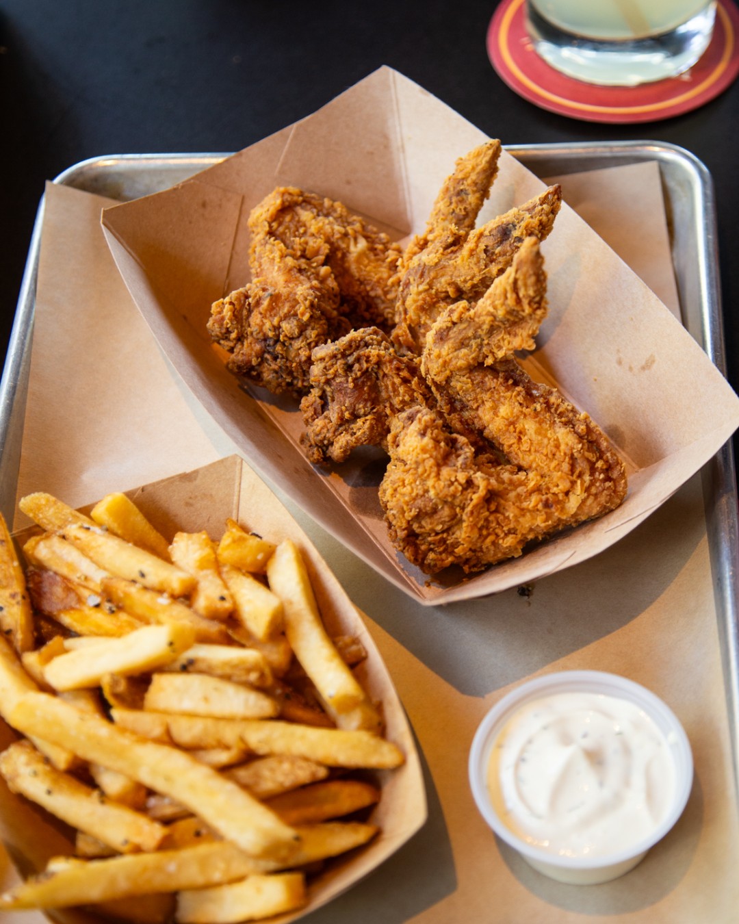 Fried chicken pieces, french fries, and white dipping sauce on a tray.