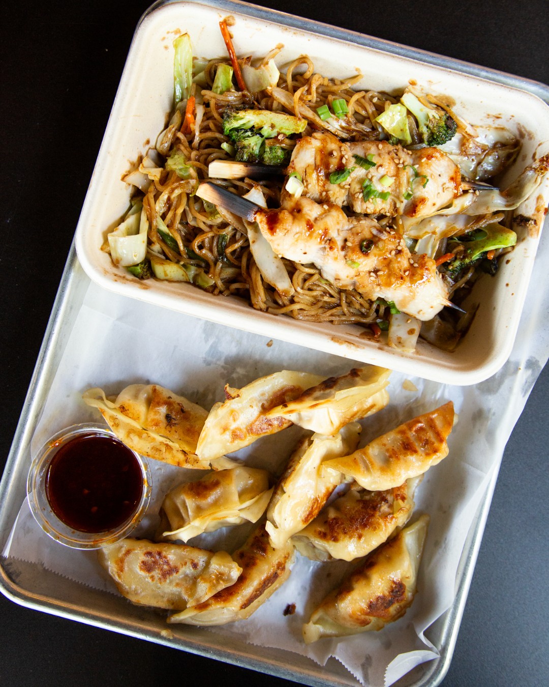 Stir-fried noodles, chicken skewers, and pan-fried dumplings with dipping sauce.