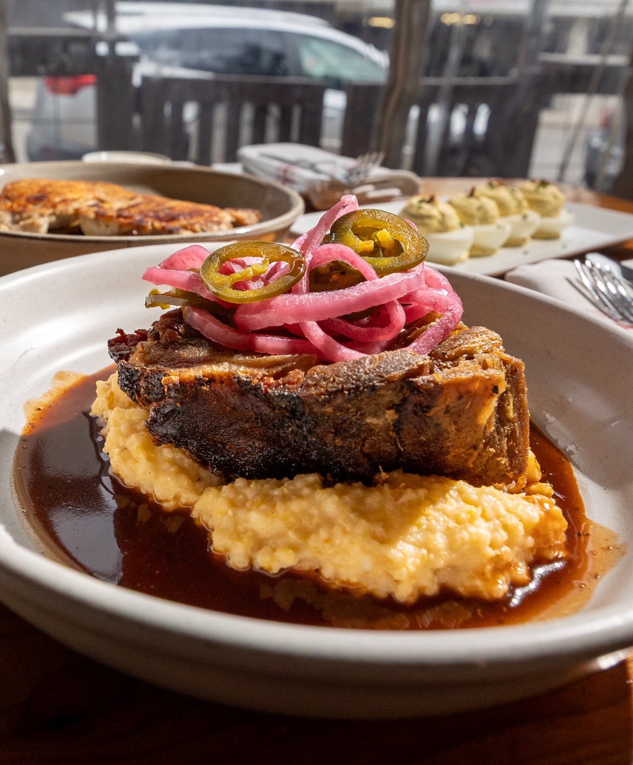 Dish of braised meat, grits, pickled onions, jalapeños, and brown sauce.