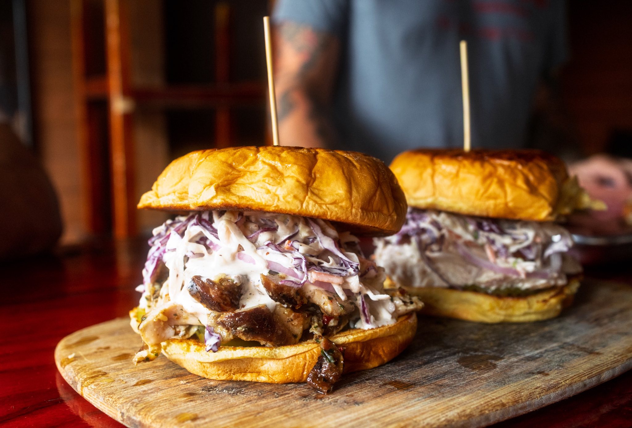 Two sandwiches with coleslaw and meat on a wooden board.