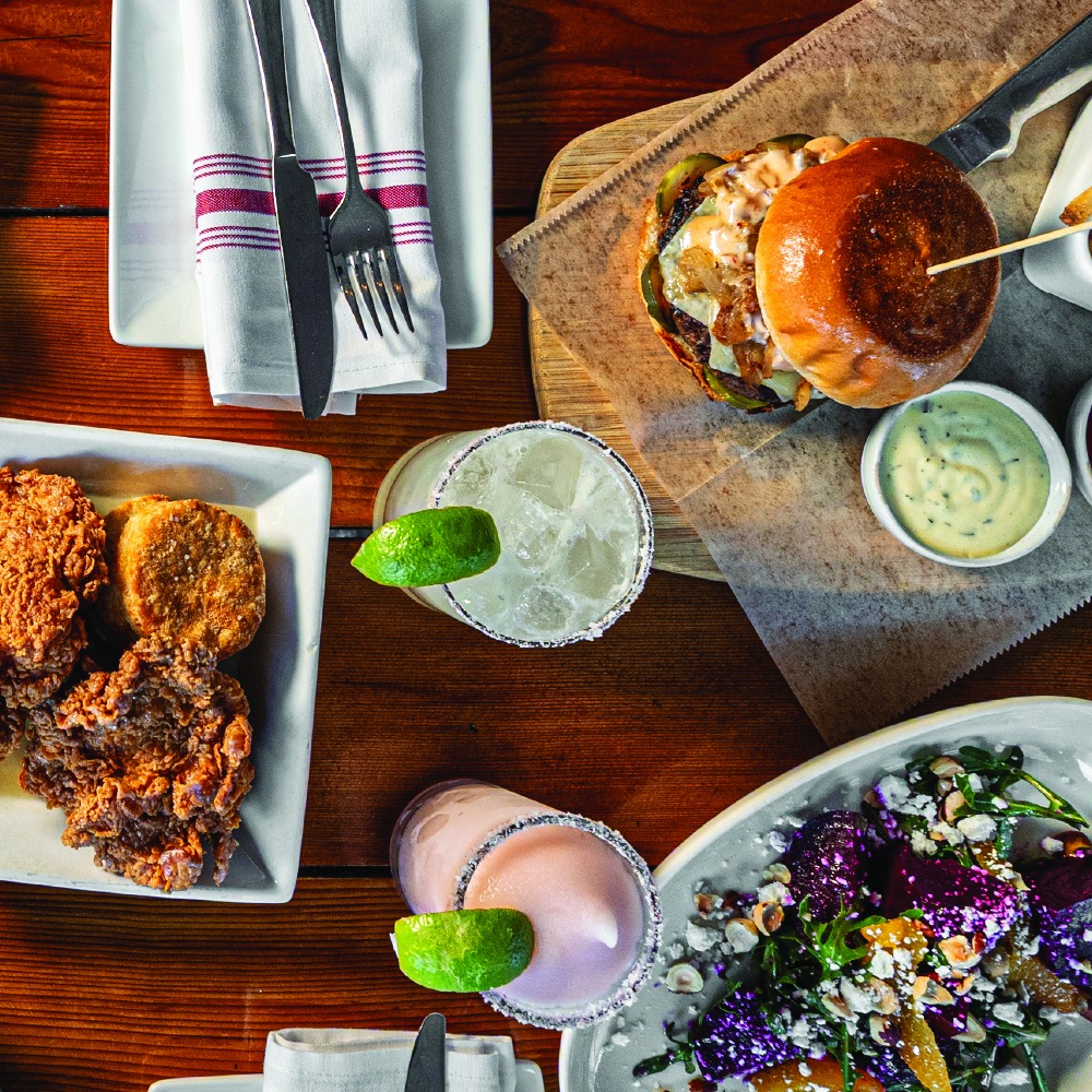 Overhead view of a meal with burger, fried chicken, salad, margaritas.