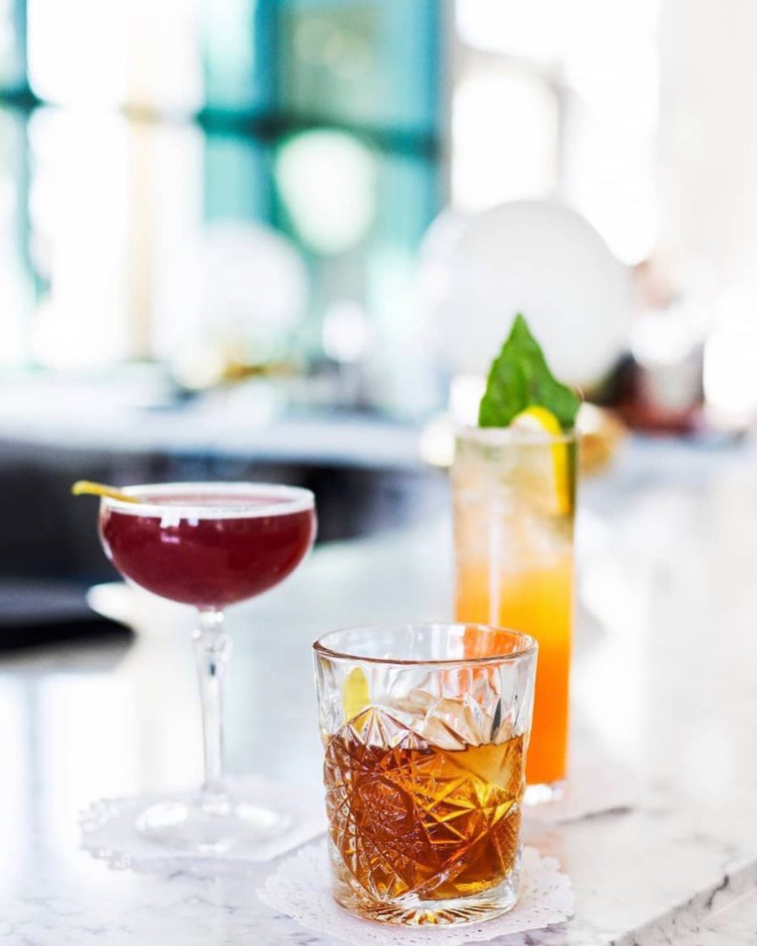 Three different cocktails in various glasses on a white bar.