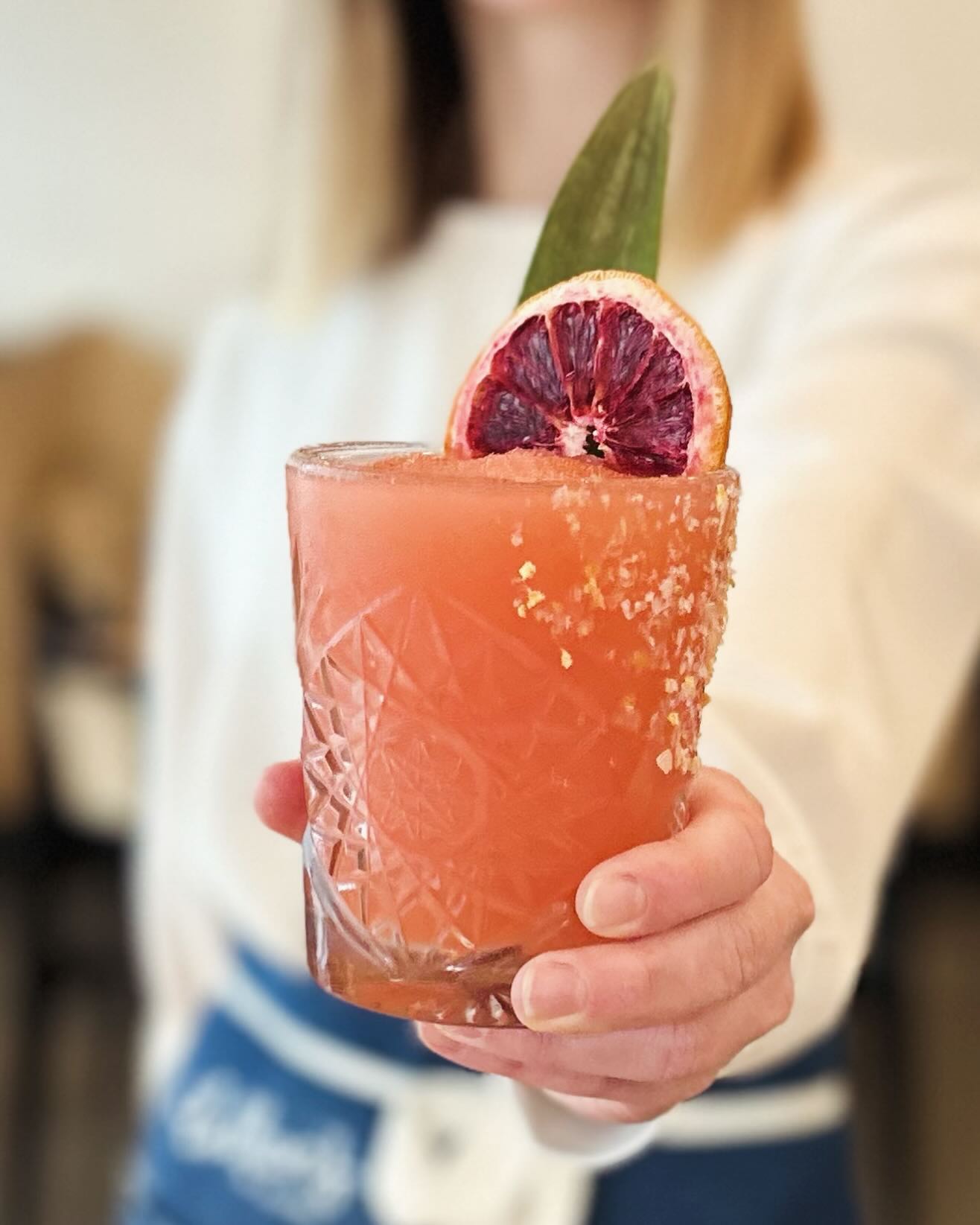 Hand holding a cocktail with blood orange garnish and salted rim.