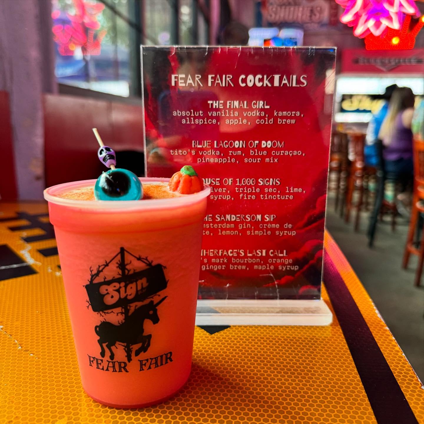 Orange drink with skull, eyeball, pumpkin garnishes, near Fear Fair menu.