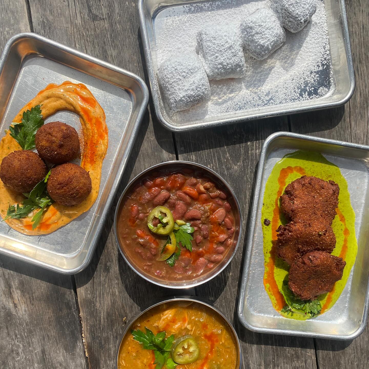 Various fried items, stews, and powdered sugar pastries on a wooden table.