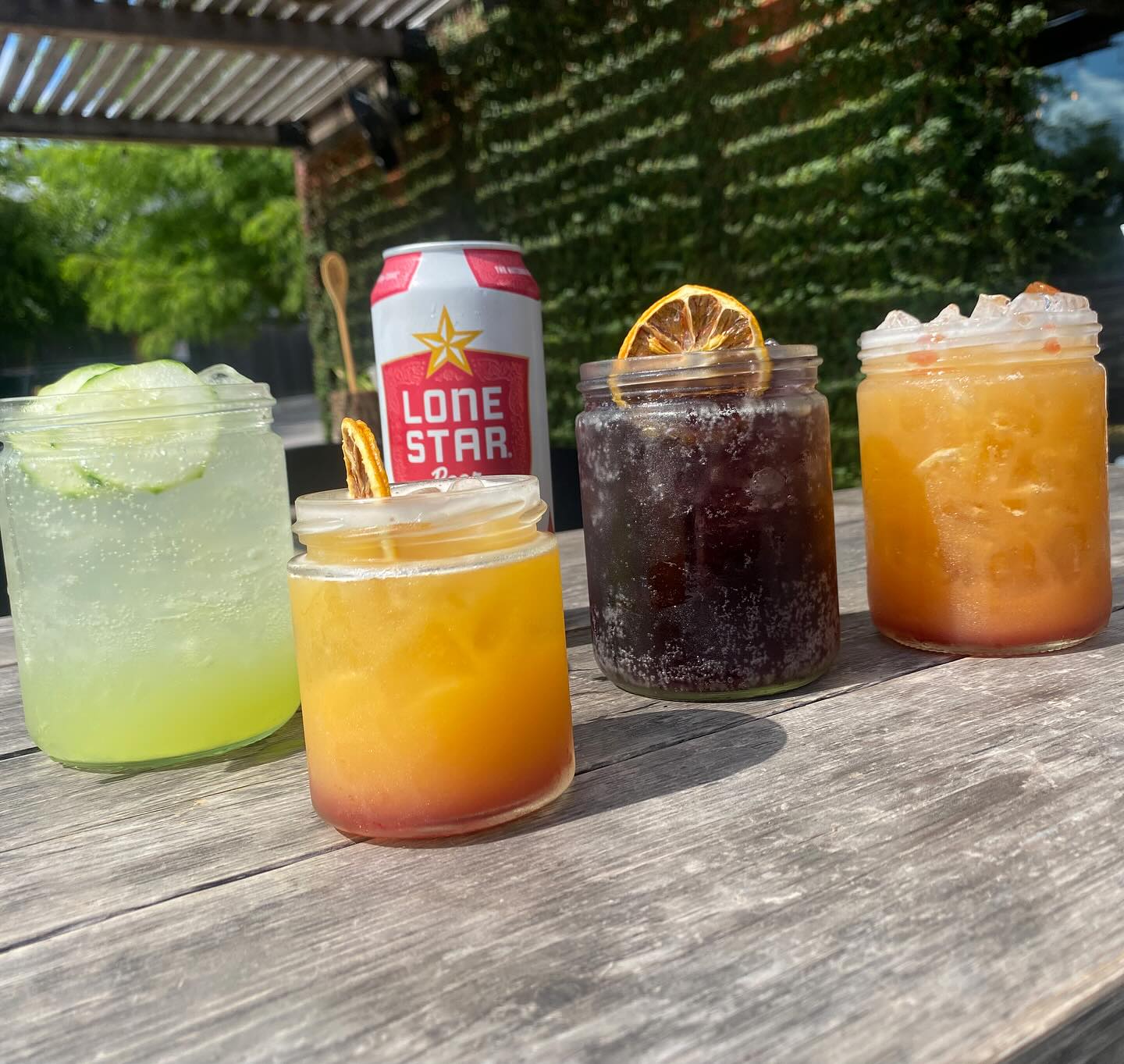 Four drinks in jars, Lone Star beer can on wooden table.