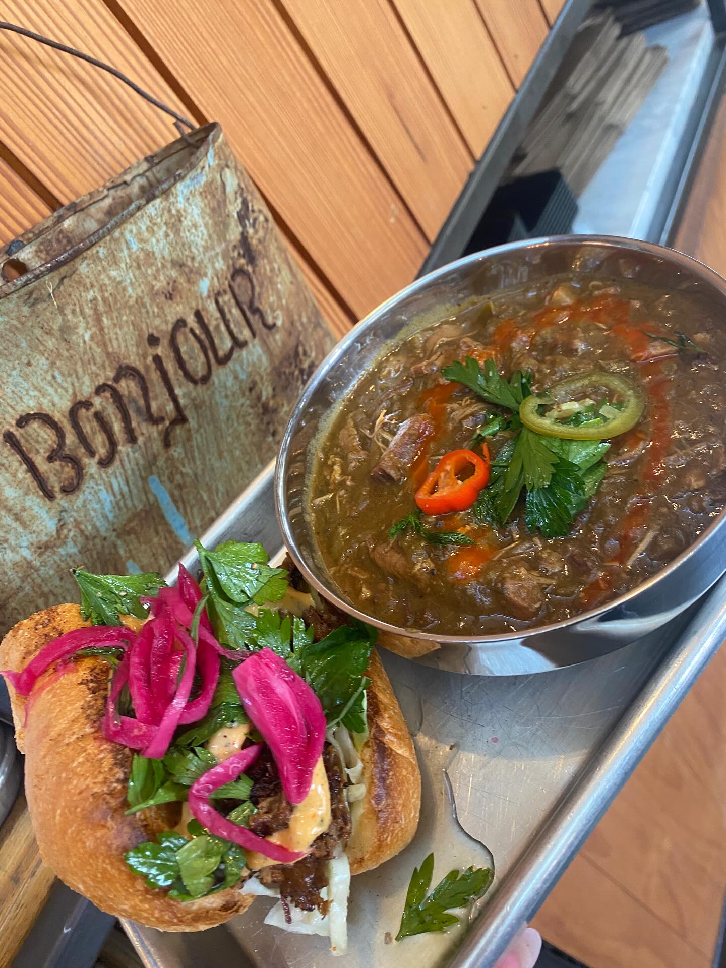 Sandwich with pickled onions and a bowl of stew on a tray.