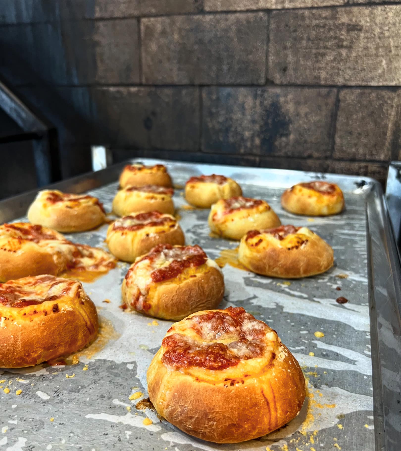 Tray of baked mini pizza buns with red sauce and cheese.