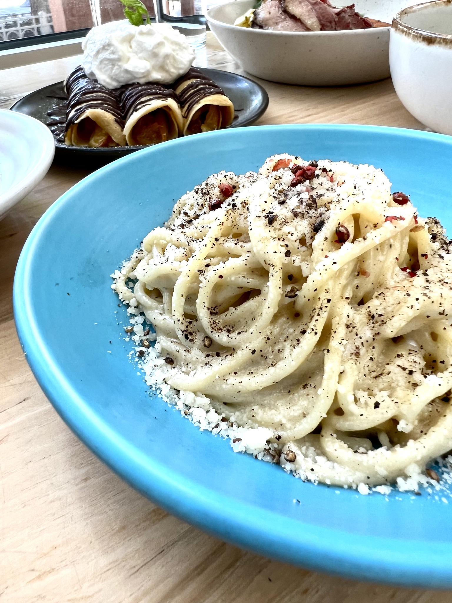 Pasta with cheese, black pepper, and red flakes in a blue bowl.