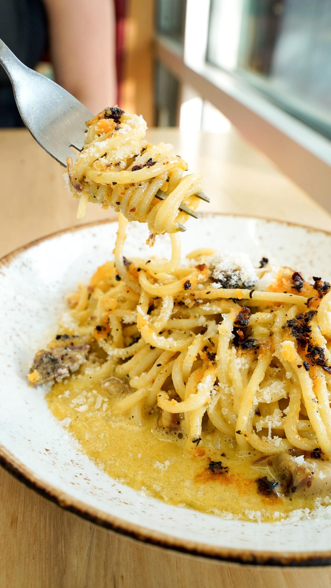 Fork lifts spaghetti with cheese and dark seasoning from a bowl.
