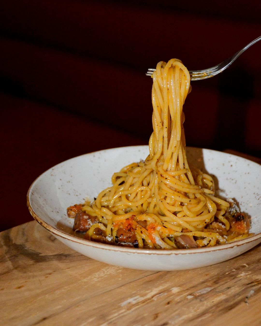 Fork lifting orange spaghetti with roe from a white bowl.