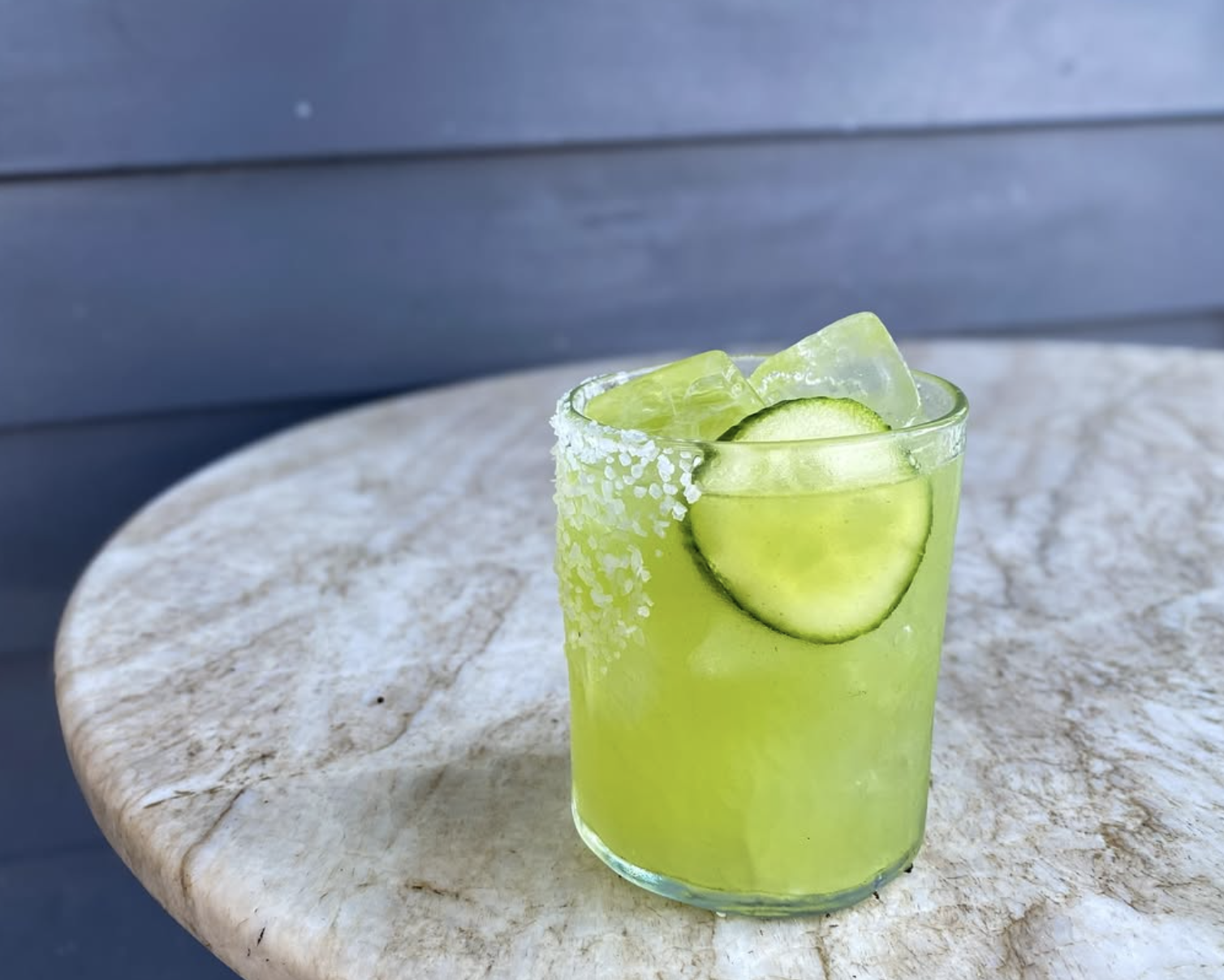 Green drink with ice, cucumber slice, and a salted rim on a table.