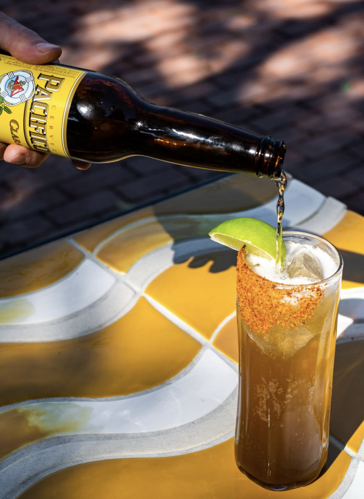 A hand pours beer into a tall drink with a lime wedge.