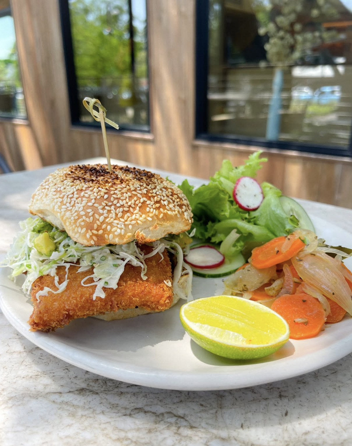 Breaded fish sandwich, side salad, cooked vegetables, and lime wedge.