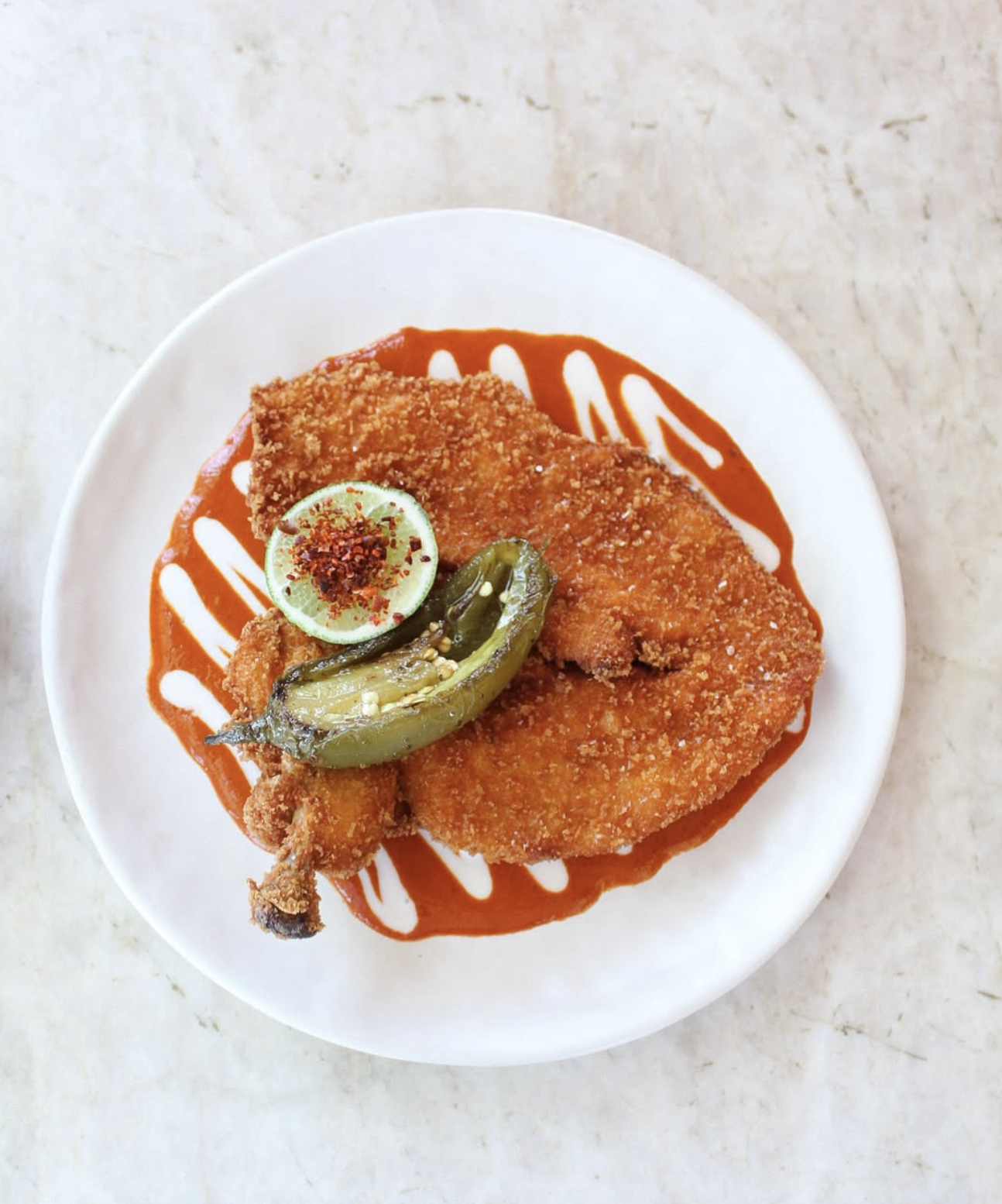 Fried breaded pieces on red sauce, with lime, chili flakes, charred pepper.