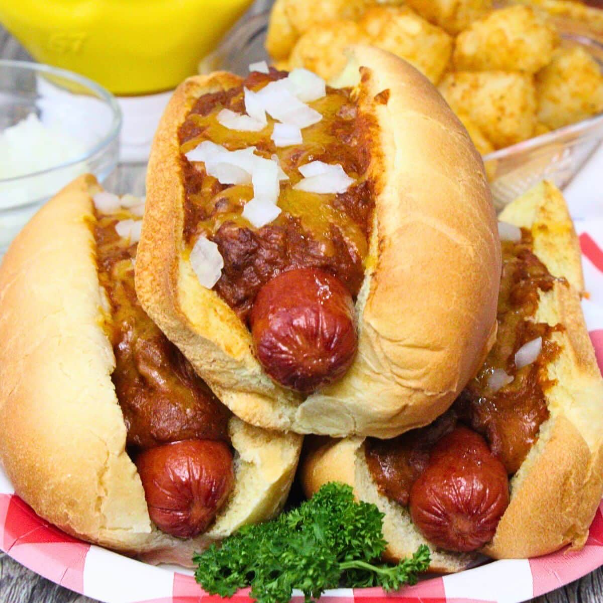 Plate of three chili hot dogs with cheese, onions, and tater tots.