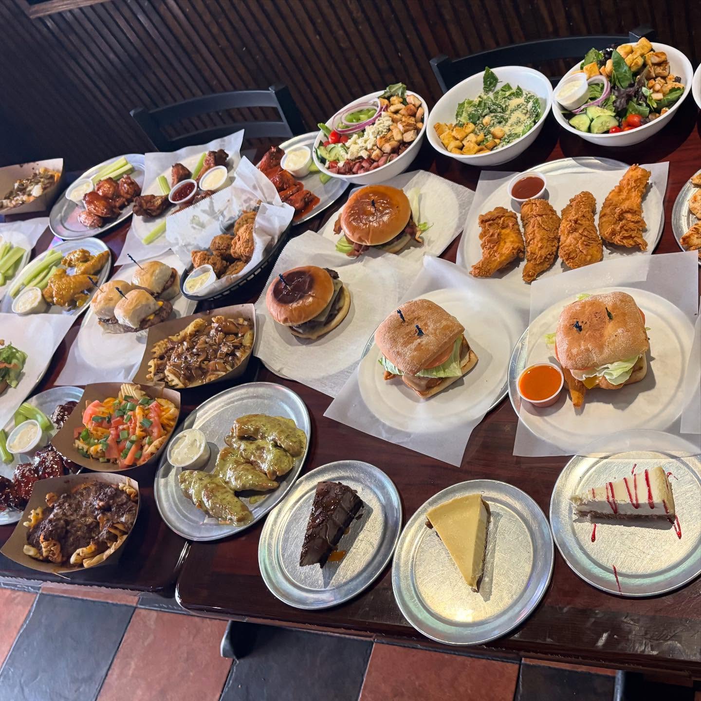 Table piled high with burgers, chicken, fries, salads, and desserts.